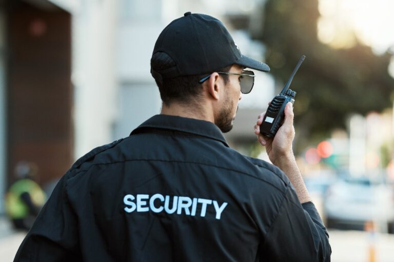 Funkgerät, Mann und ein Wachmann oder Sicherheitsbeauftragter im Freien auf einer städtischen Straße zur Kommunikation. Rücken einer Person mit einem Walkie-Talkie auf einer städtischen Straße, um ein Verbrechen zur Untersuchung und Überwachung zu melden